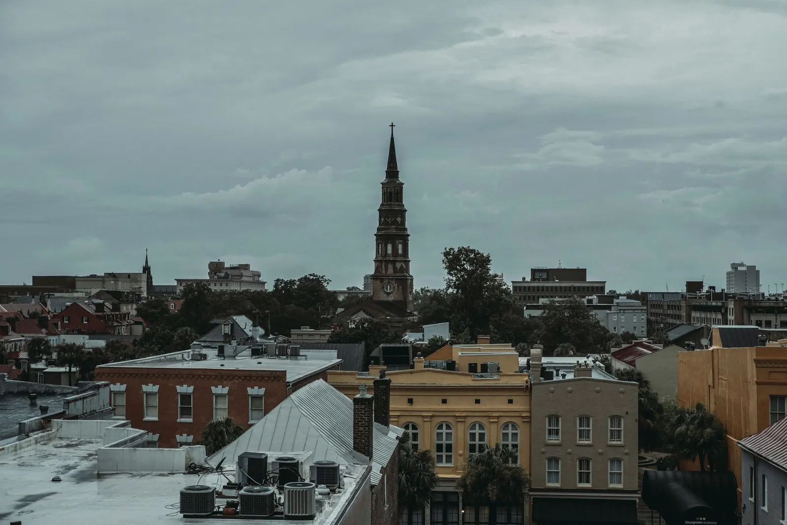Rooftops of downtown Charleston under a grey sky with a church steeple rising above them.