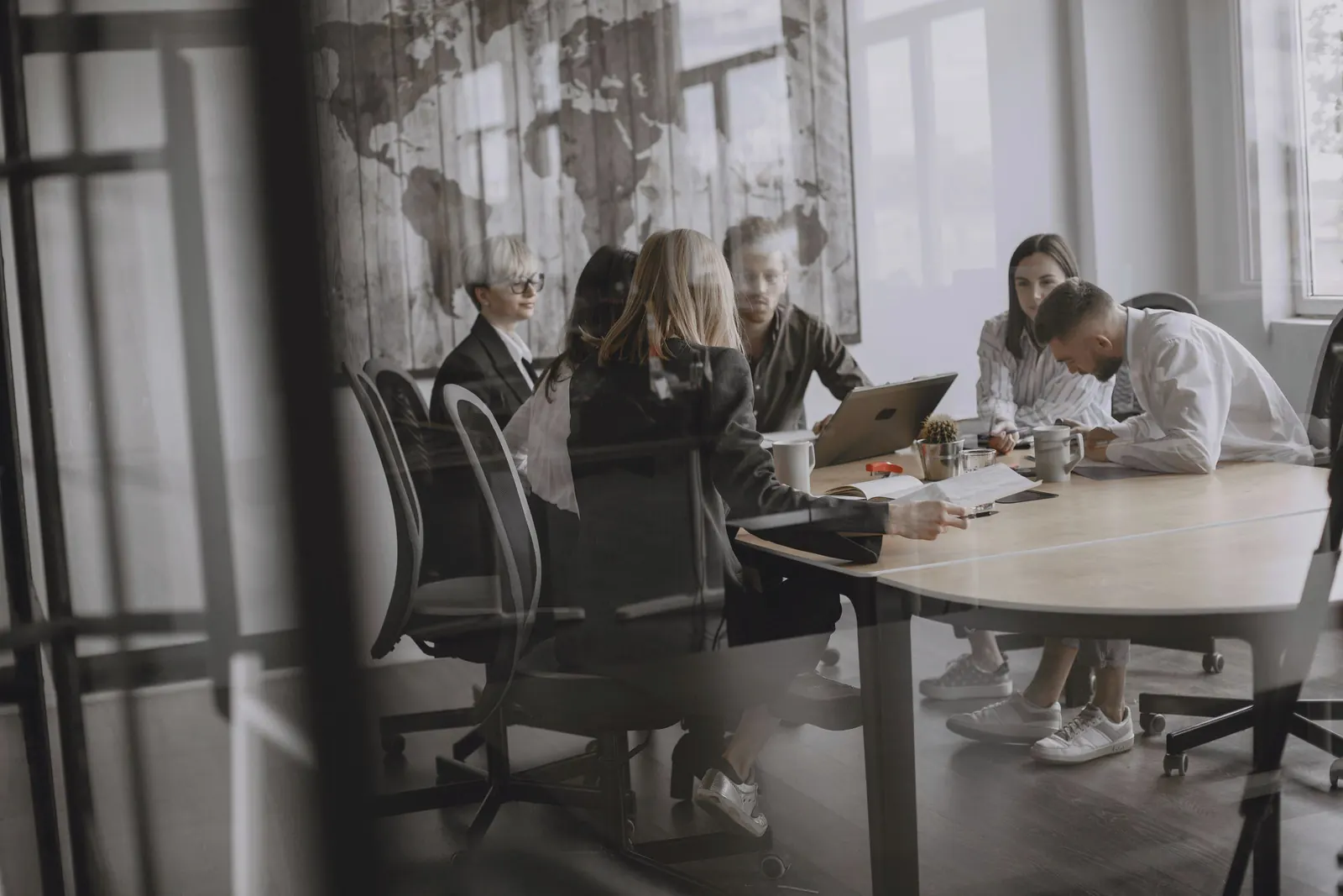 A team meeting around an oval table, seen from a distance through a glass partition.