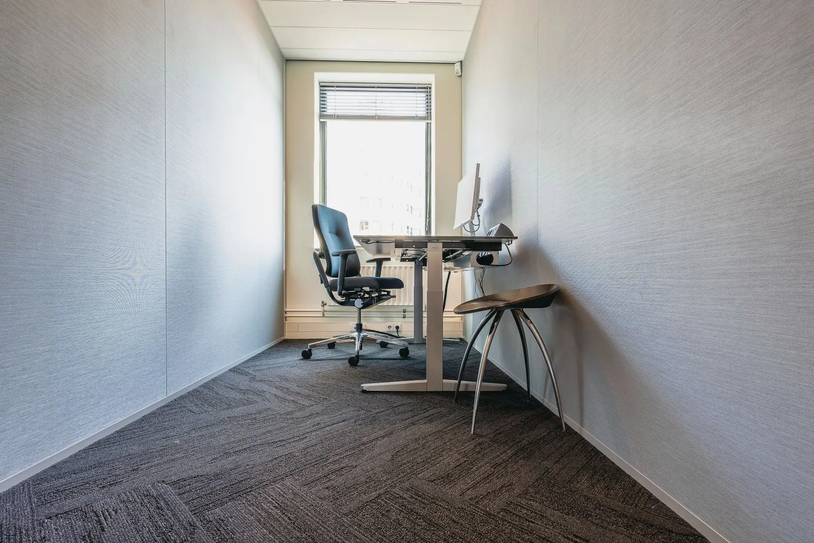 A small quiet office with a single desk and chair facing a bright window.