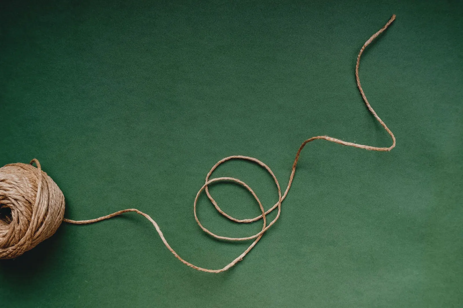 A ball of natural twine with a loose strand looping across a deep green surface.